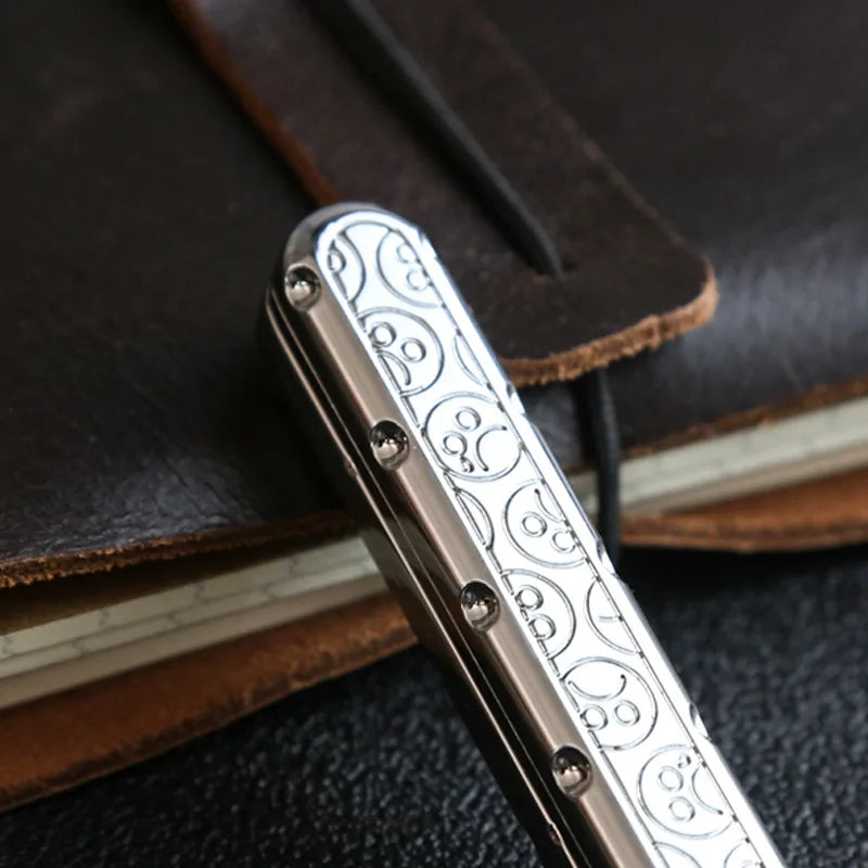 A close-up of a silver metal fidget slider with intricate patterns resting on a brown leather notebook.