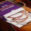 A box of coated acoustic guitar strings in bronze color is shown next to a wooden guitar.