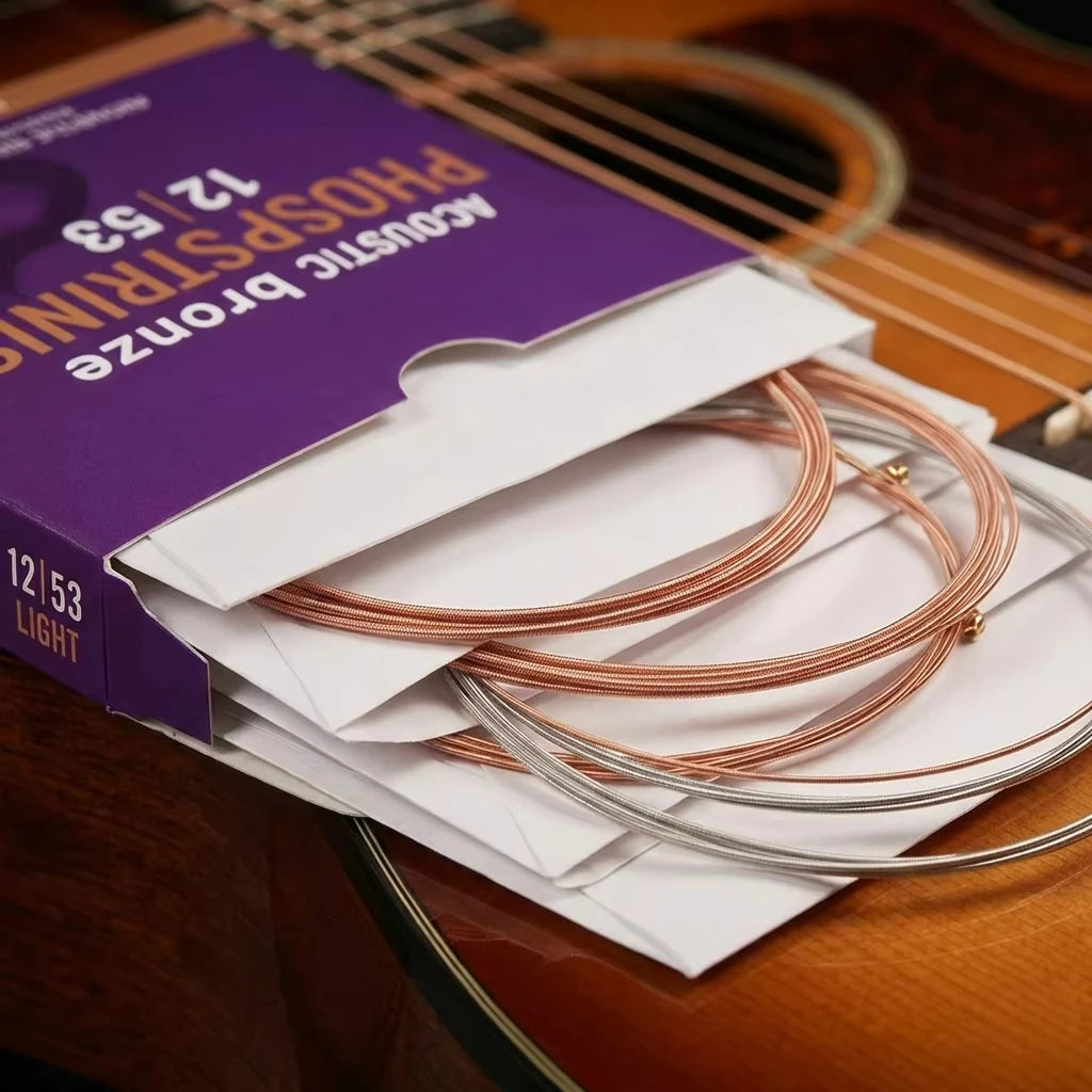 A box of coated acoustic guitar strings in bronze color is shown next to a wooden guitar.