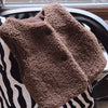 A brown, fluffy fleece vest is displayed on a patterned surface.
