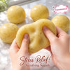 Hands squeeze a yellow mashed potato squish toy stress reliever with several other toys in the background.