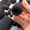 A hand holds a black replacement microphone foam cover, showing its texture and size against other similar covers.