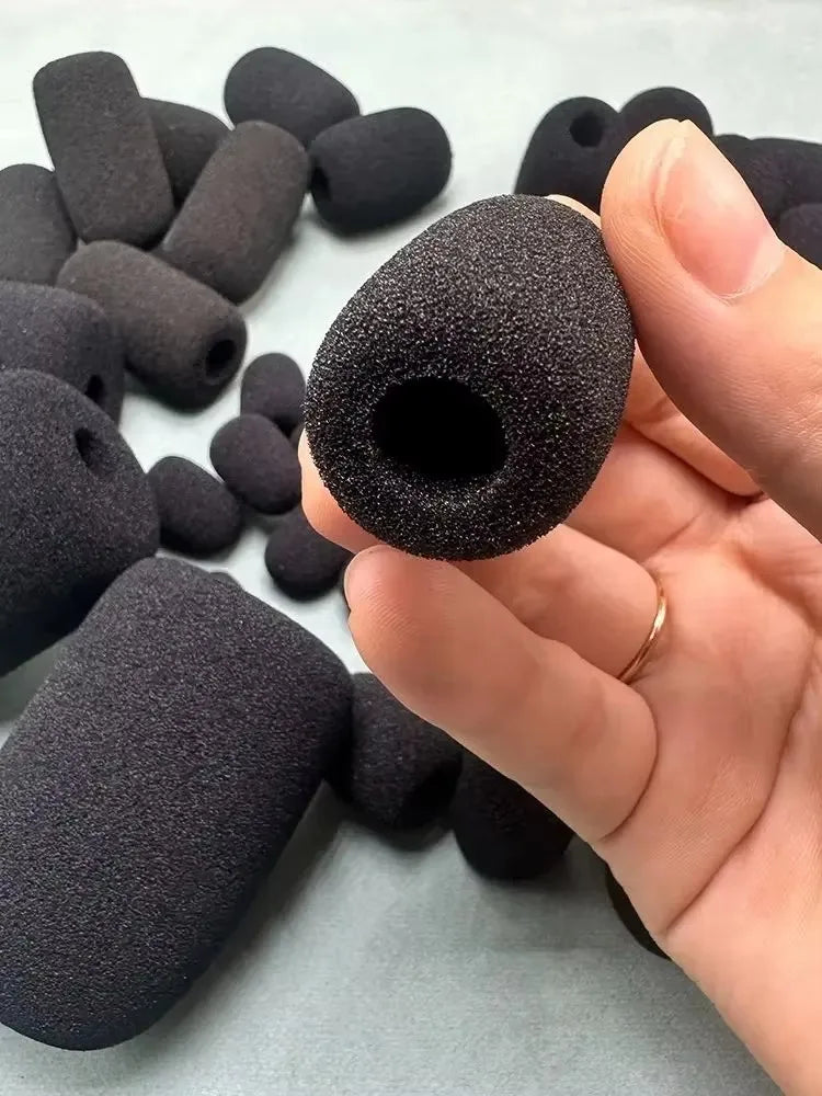 A hand holds a black replacement microphone foam cover, showing its texture and size against other similar covers.