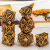 A stack of seven metal dice in gold and black designs for tabletop role-playing games