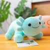 A soft, light blue axolotl plush toy is lying on a wooden surface next to a piece of paper.