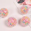 A close-up of a rainbow squishy stress relief ball with multicolored, textured surface resting on a white background.