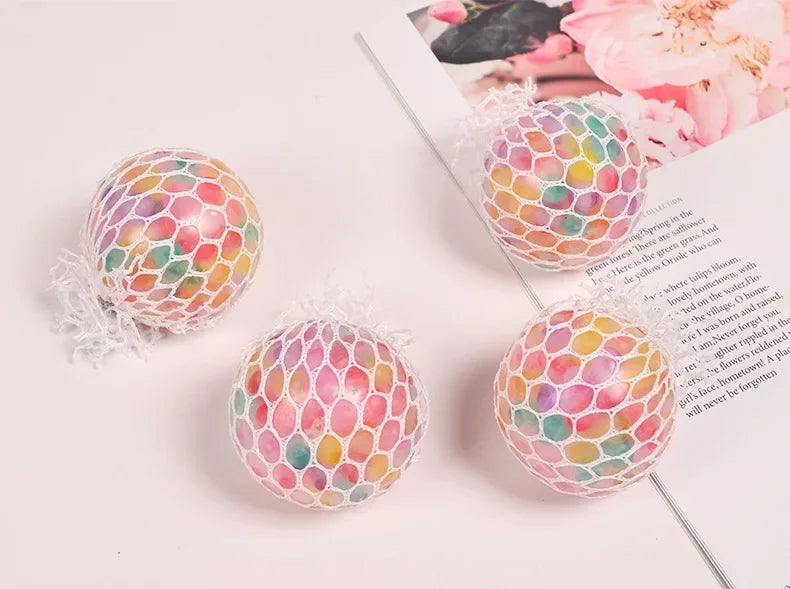 A close-up of a rainbow squishy stress relief ball with multicolored, textured surface resting on a white background.