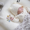 A baby is sleeping on a white fluffy surface, holding a silicone teether with colorful beads.