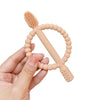A hand holds a soft silicone baby teether with easy-grip handles, showing the textured silicone teeth and rounded grips.