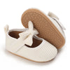 A pair of white lace-trimmed baby girl moccasin shoes with bows and tan textured soles.