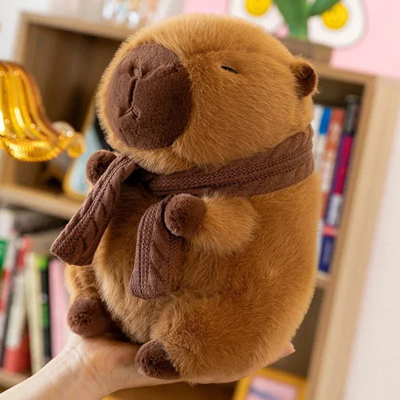 A brown plush capybara stuffed animal wearing a knitted brown scarf, held in a hand.