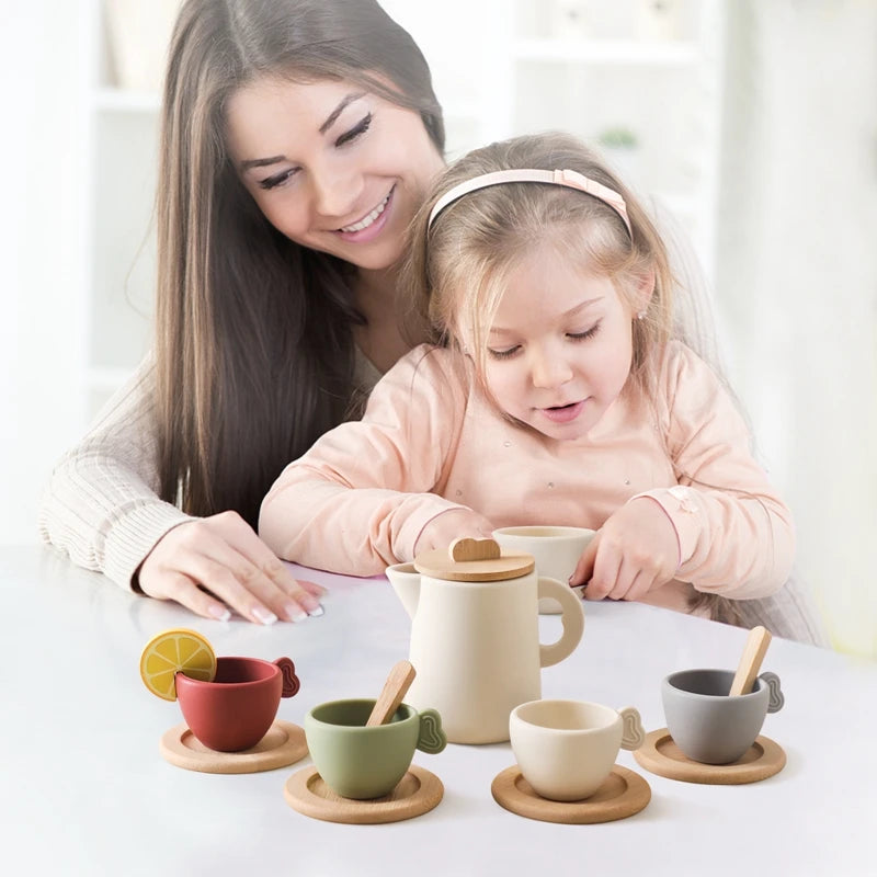 A young girl and woman are setting up a wooden pretend play tea party set with various cups and saucers.