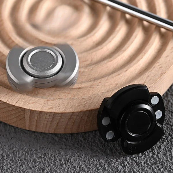 A close-up of a silver stainless steel fidget spinner and slider resting on a light wooden surface.