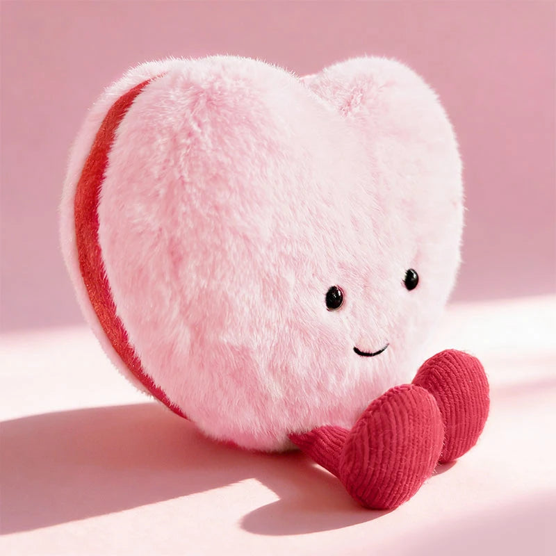 A pink heart-shaped plush cushion with a red stripe and a knitted pink accent.
