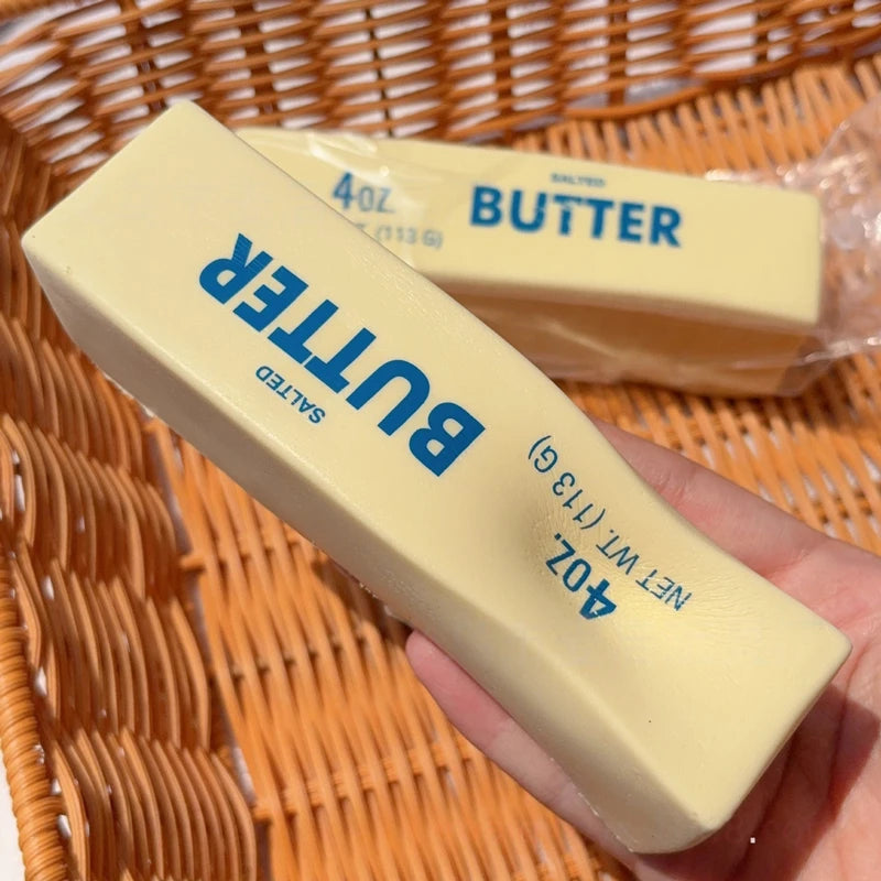 A hand holds a yellow butter stress relief toy packaged in plastic against a woven basket background.