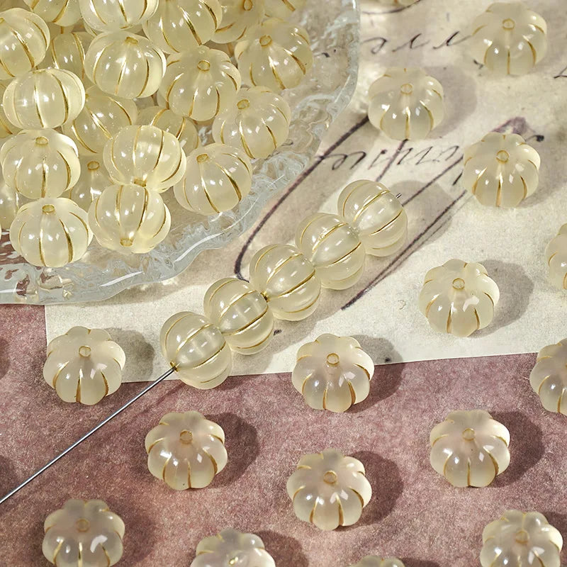 A collection of small, translucent gold-traced pumpkin resin beads for jewelry making scattered on a textured surface.