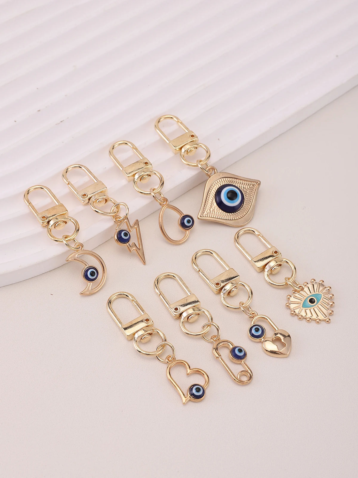 A set of gold-toned cartoon evil eye keychains with blue accents displayed on a white background.