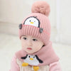 A baby wearing a pink knit penguin hat and matching scarf set