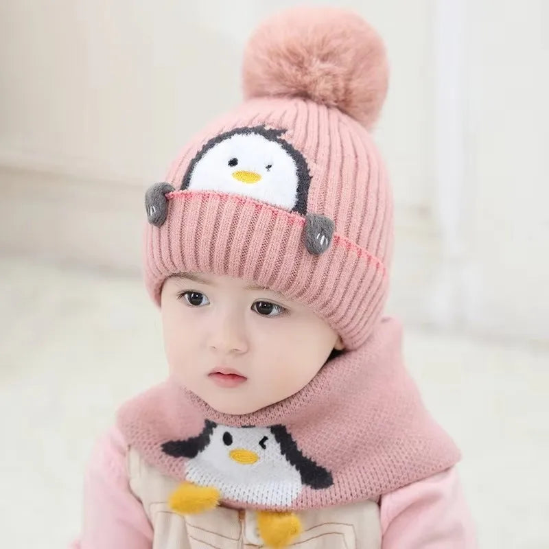 A baby wearing a pink knit penguin hat and matching scarf set