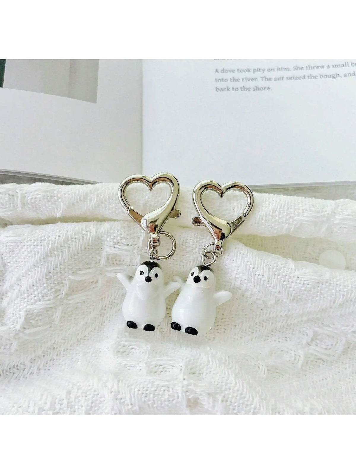 A set of two white penguin heart keychains attached to a silver-colored chain, displayed on a white textured cloth.