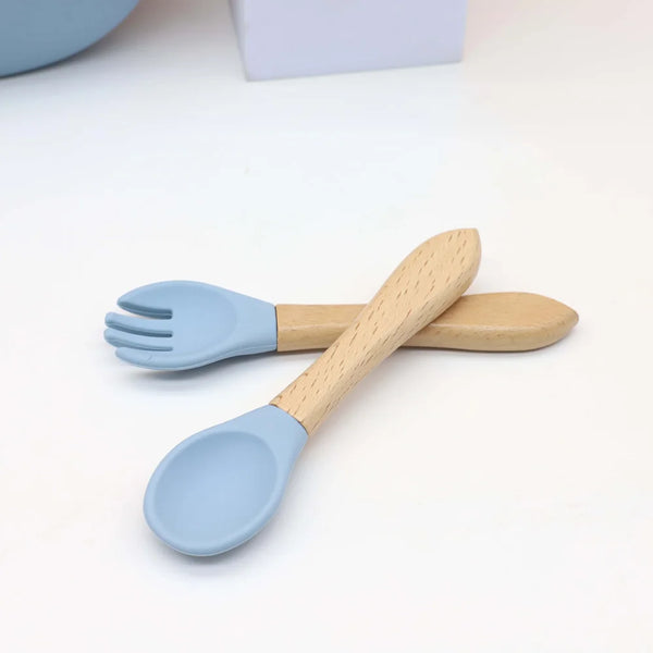 Service à bébé en silicone bleu clair avec cuillère et fourchette sur une surface blanche.