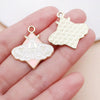 Gold-toned butterfly drop charm with a geometric pattern and pink enamel on a hand.