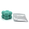 A pile of teal colored candle dye chips for wax, next to a sealed plastic bag.