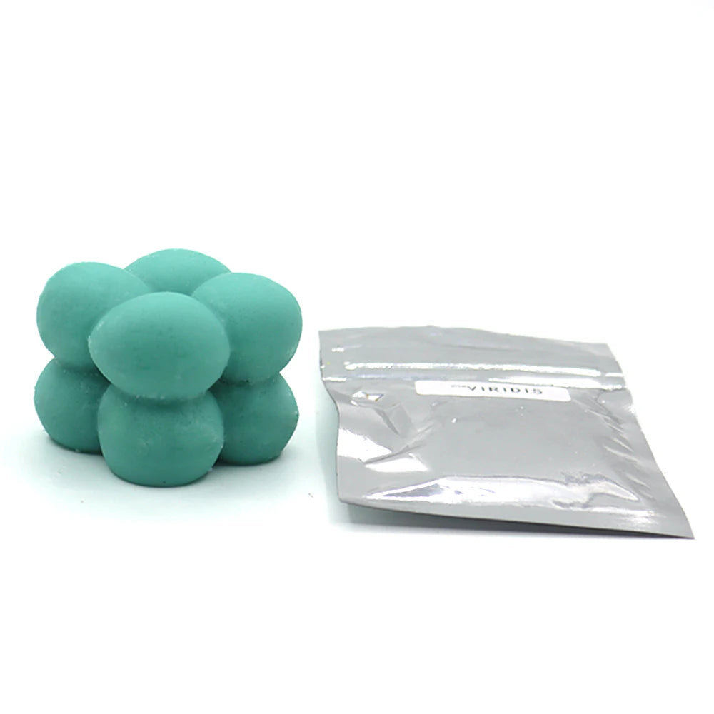 A pile of teal colored candle dye chips for wax, next to a sealed plastic bag.