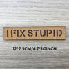 Un patch rectangulaire marron tissé avec le texte IFIXSTUPID, montré sur un fond en bois clair.