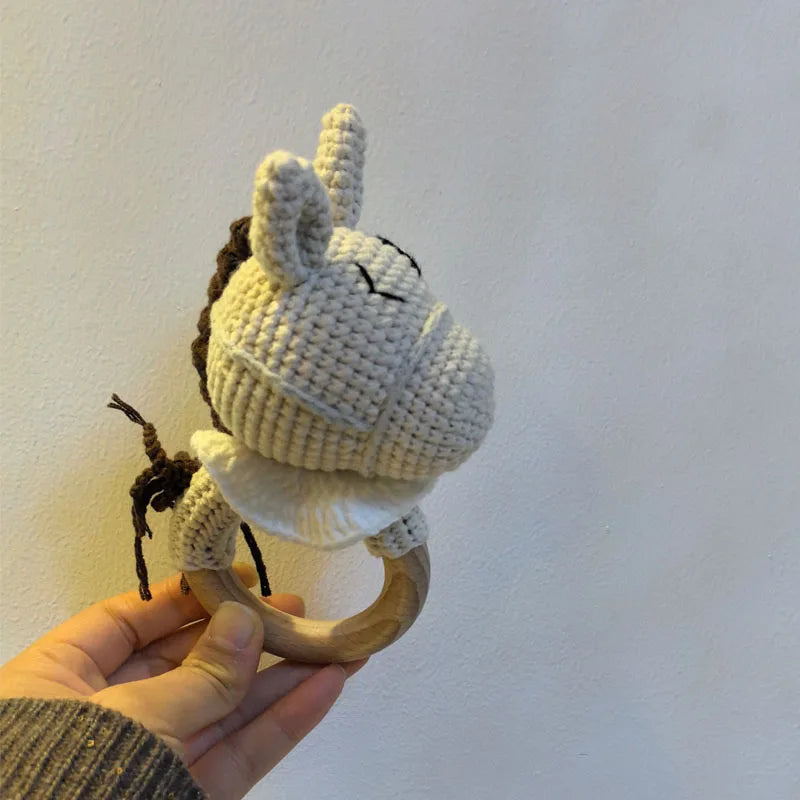 A hand holds a crocheted otter baby rattle and teether ring made of light beige yarn.