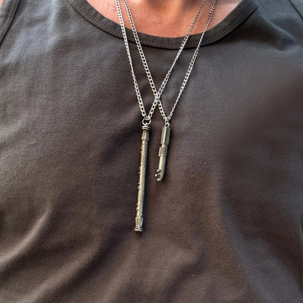 A close-up of a silver chain necklace with a mini metal saber keychain pendant worn against a dark shirt.