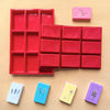 A red silicone mold tray with multiple cavities and several small colored silicone molds for DIY crafts