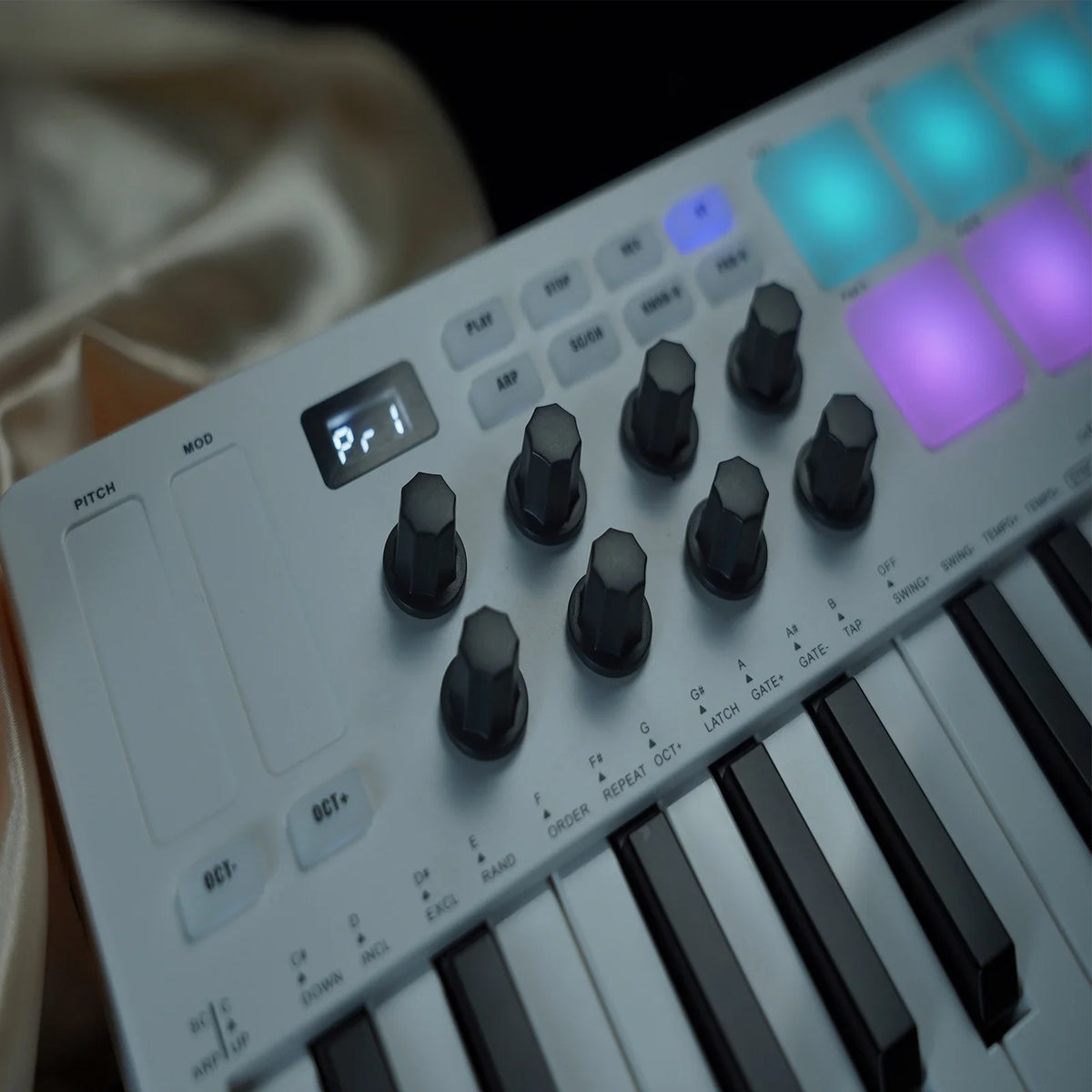Close-up of a white MIDI keyboard controller with black keys and illuminated blue and purple pads.
