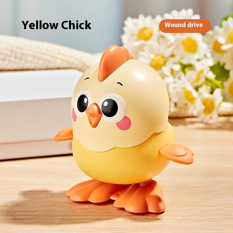 A yellow chick wind-up toy with orange accents sitting on a wooden surface next to white and floral elements.