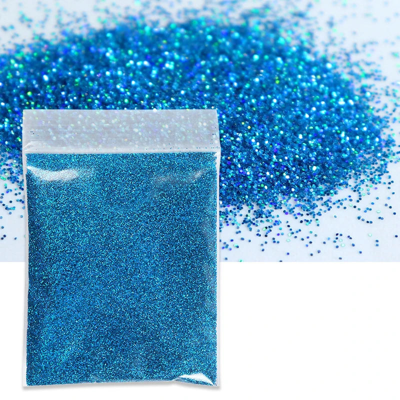 A sealed packet of bright blue holographic glitter powder next to a pile of loose glitter.