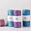 Three spools of metallic yarn in teal, purple, and blue are displayed on a white surface.
