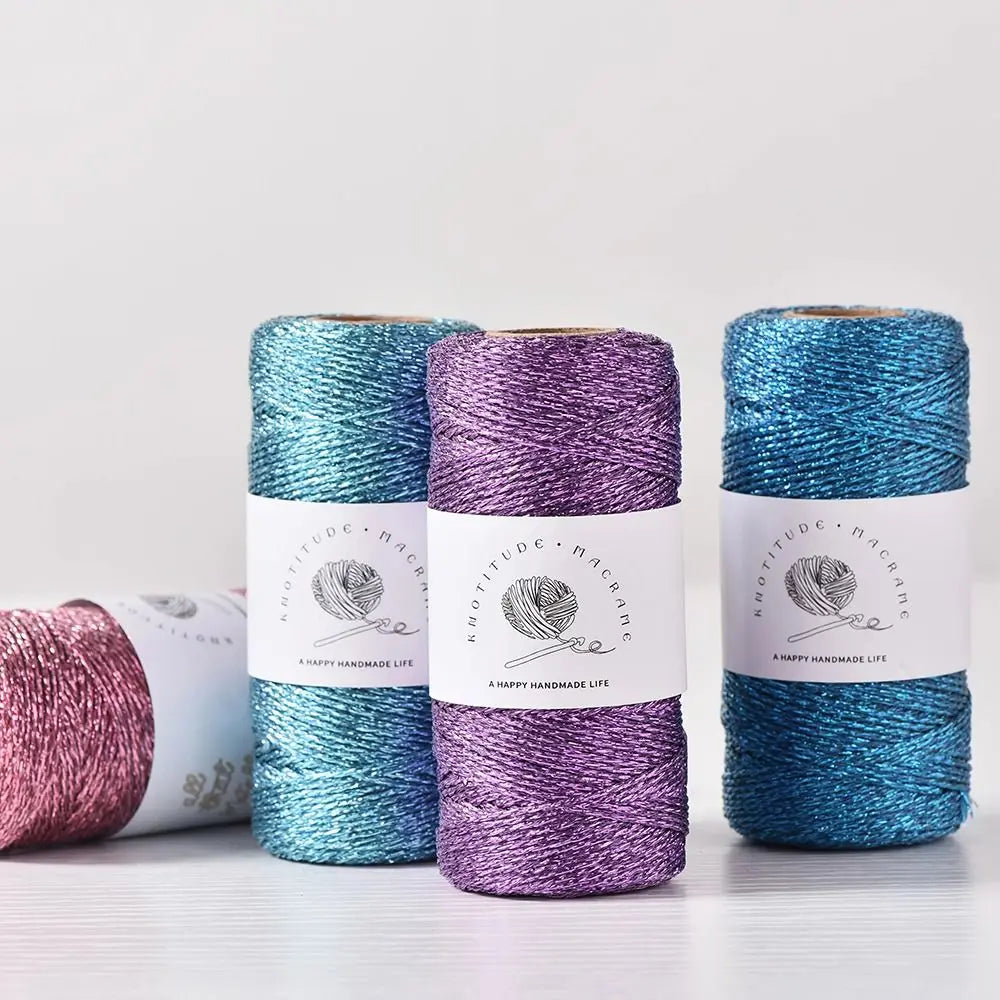 Three spools of metallic yarn in teal, purple, and blue are displayed on a white surface.