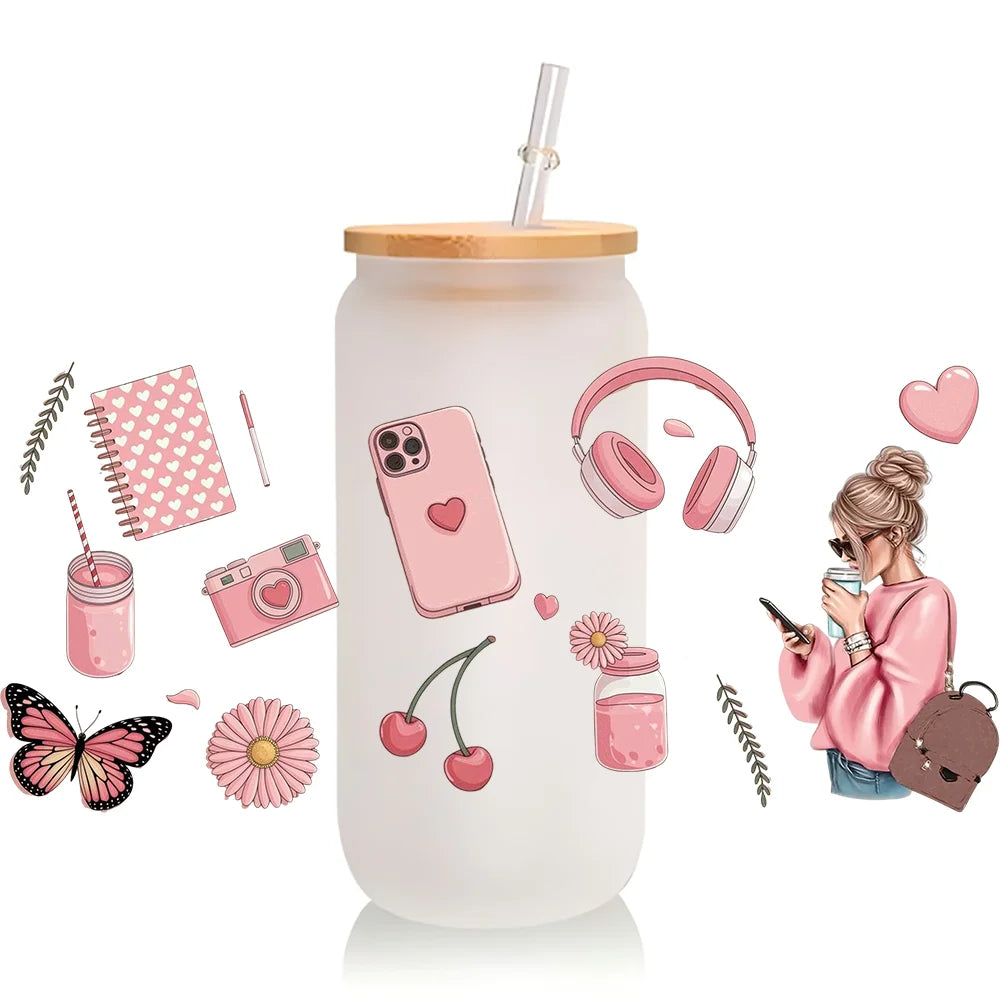 A clear tumbler with a pink heart design featuring various makeup-themed elements like a lipstick, camera, and headphones.
