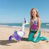 Une jeune fille portant une robe de oie-sirène avec des écailles violettes et vertes sur une plage de sable.