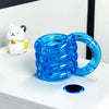 A bright blue crystal fidget twist rope is shown next to a white cat figurine on a white surface.