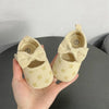 A pair of beige soft sole sandals for a baby, featuring a bow detail and small yellow stars on the sole.