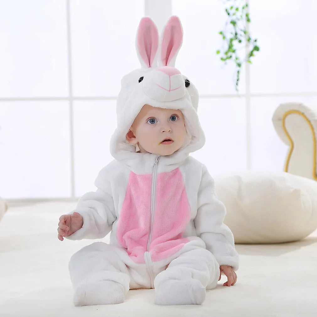 A baby wearing a white and pink animal hooded romper with long ears, sitting on a light surface.