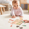 A baby is interacting with a wooden Montessori shape sorting puzzle, placing various wooden shapes on a white surface.