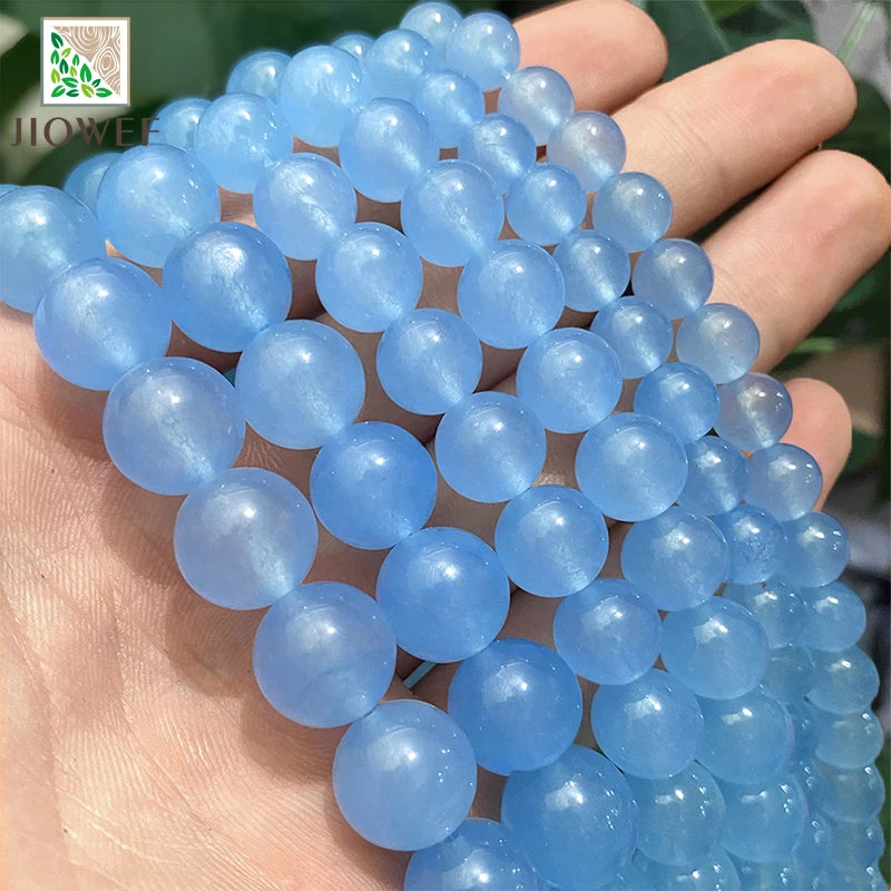 A hand holds a strand of natural light blue chalcedony beads used for jewelry making.