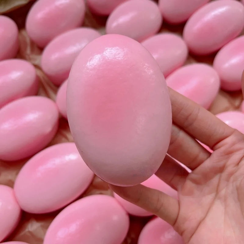 A hand holds a pink cheese-shaped squishy stress relief toy among many similar toys.