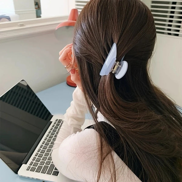 A woman with long dark hair is using an elegant acetate hair claw clip to secure her hair.