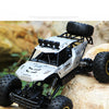 A white and black high-speed 4WD off-road RC truck with large tires is positioned on a light-colored rock.