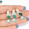 Gold-plated enamel charms depicting a mermaid figure with green and white scales on a hand.