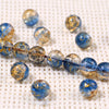 A string of gradient blue crystal glass beads with a golden crackle finish resting on a white textured surface.