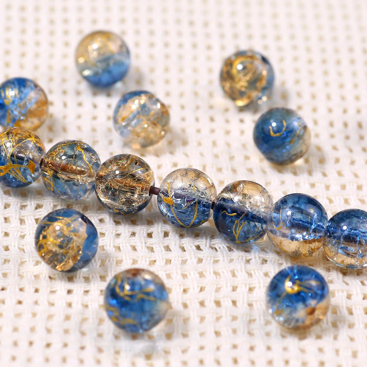 A string of gradient blue crystal glass beads with a golden crackle finish resting on a white textured surface.